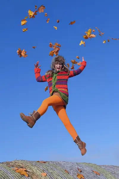 Woman jumping in air having fun with leaves